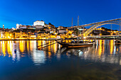 Blick über die traditionellen Rabelo Boote am Douro Ufer in Vila Nova de Gaia auf die Altstadt von Porto und die Brücke  Ponte Dom Luís I in der Abenddämmerung, Vila Nova de Gaia, Portugal, Europa