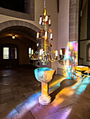 Holy water font with historic candlestick in the sun shining through a colorful church window, St. Johann Baptist, Bad Honnef, North Rhine-Westphalia, Germany