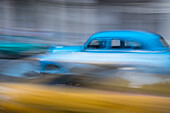 Cuba, Havana. Classic cars speed by in a blur along the streets of the city.