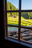 Blick aus einem Fenster auf eine Hütte, eingebettet in die Hügel der österreichischen Alpen