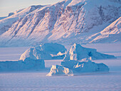 Eisberge, die im Winter im Meereis des Uummannaq-Fjordsystems eingefroren sind. Hintergrund ist die Halbinsel Nuussuaq, Grönland, Dänemark.