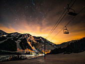 USA, Washington State, Pierce County, Crystal Mountain Resort. Chairlift in front of starry dusk sky as sun sets behind mountains.