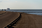People walking by the North Sea in the province of Zeeland in the Netherlands, with a cargo ship on the backgroud.