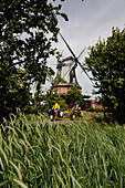 Cyclists in front of the windmill near Borgsum, Foehr Island, North Friesland, North Sea, Schleswig-Holstein, Germany, MR