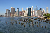 Blick vom Bridge Park in Brooklyn über Holzpfähle der Old Pier 1, den East River und auf die Südspitze des Financial District von Lower Manhattan, New York, New York, USA