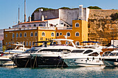 Several large luxury yachts are moored in front of a fort at the port of Mahon, Menorca, Balearic Islands, Spain