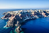 Luftaufnahme einer Insel im tiefblauen Meer der Ägäis, Felsformationen, weiß getünchte Häuser, die auf den Klippen thronen.