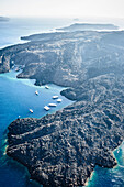 Aerial view of the landscape of an island in the caldera, volcanic rock and steep cliffs and sheltered moorings with boats.