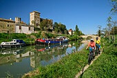 Zwei Personen fahren am Canal du Midi Rad, Colomiers im Hintergrund, Canal du Midi, UNESCO Welterbe Canal du Midi, Okzitanien, Frankreich