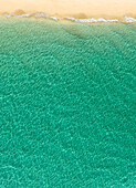 Blick von oben auf das türkisfarbene Meer und den Strand