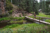 USA, New Mexico, Jemez Mountains, Woman walking on wooden bridge over stream