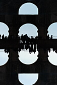 Double exposure of tourist silhouettes seen in the arches of the Colosseum in Rome, Italy.