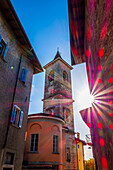 Altstadt mit altem Haus und Kirchturm mit Sonnenstrahl und Lens Flare an einem sonnigen Tag in Arzo, Tessin, Schweiz.