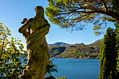 Statue mit Blick auf die Lombardei in Italien und den Luganersee mit Berg und blauem Himmel von Morcote, Tessin, Schweiz.