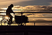 Silhouette einer Person die mit einem Lastenfahrrad über die Brücke fährt bei Sonnenuntergang, Kopenhagen, Dänemark, Europa