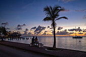 Couple on bench, palm tree, sailboat and World Voyager (nicko cruises) expedition cruise ship at pier at sunset, Kralendijk, Bonaire, Netherlands Antilles, Caribbean