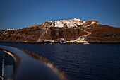 Railings on deck of expedition cruise ship World Explorer (Nicko Cruises) with Oia cliff houses in the distance at dusk, Santorini, South Aegean, Greece, Europe