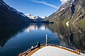 Couple on the bow of expedition cruise ship World Voyager (Nicko Cruises) in Sunnylvsfjorden, near Stranda, Møre og Romsdal, Norway, Europe