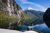 Paar am Bug von Expeditionskreuzfahrtschiff World Voyager (nicko cruises) im Geirangerfjord mit Seven Sisters Wasserfall, Geiranger, Møre og Romsdal, Norwegen, Europa