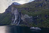 Luftaufnahme von Expeditionskreuzfahrtschiff World Voyager (nicko cruises) vor dem Seven Sisters Wasserfall im Geirangerfjord, Geiranger, Møre og Romsdal, Norwegen, Europa