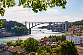 View of the riverbank and a backlit Douro Bridge seen from the Jardim do Palácio in the Arrábida district of Porto, Portugal