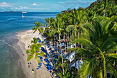 Luftaufnahme von Kokospalmen und Menschen die sich am Strand entspannen mit dem Expeditionskreuzfahrtschiff World Voyager (nicko cruises) in der Ferne, Isla Tortuga, Puntarenas, Costa Rica, Mittelamerika
