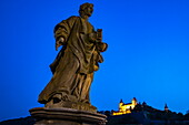 Statue auf der Alten Mainbrücke über den Main mit beleuchteter Festung Marienberg in der Abenddämmerung, Würzburg, Franken, Bayern, Deutschland, Europa