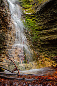 Waterfall long exposure in the forest at Burschenplatz in Rautal with red leaves and branches in the foreground, Jena, Thuringia, Germany