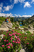 Man and woman hiking taking a break, alpine roses in the foreground, Valle Gerber, Aigüestortes i Estany de Sant Maurici National Park, Pyrenees, Catalonia, Spain