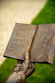 Statue holding a book with the inscription 'nooit de moed opgeven' or 'never give up'.