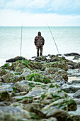 A man in camouflage clothing fishing in the sea with two perches