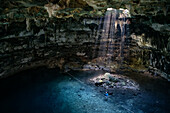 Sunbeams enter Cenote Xkeken near Valladolid through a hole in the rock ceiling, woman in water, Yucatan, Mexico, North America, Latin America