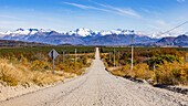 Malerisches Panorama mit Schotter Straße, die durch herbstliche Landschaft direkt auf die Berge der Anden zuläuft, Chile, Patagonien, Südamerika