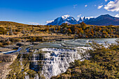Der Wasserfall und die Kaskaden am Rio Paine Fluss vor dem Bergmassiv Torres del Paine mit herbstlichen Farben, Chile, Patagonien, Südamerika