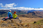 Mann und Frau beim Wandern sitzen auf Felsen und blicken über Drakensberge, Shebas Breasts, Lotheni, Kwa Zulu Natal,  Maloti-Drakensberg, Südafrika