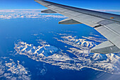 View of airplane wing and Norwegian coast with snowy islands, near Tromsö, Troms og Finnmark, Norway