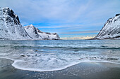 Strand von Steinfjord mit einlaufender Welle und verschneiten Bergen im Hintergrund, Steinfjord, Senja, Troms og Finnmark, Norwegen