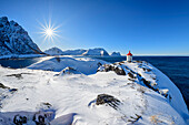Leuchtturm steht auf Landzunge mit verschneiten Bergen im Hintergrund, Senja, Troms og Finnmark, Norwegen