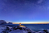 Beleuchteter Leuchtturm steht auf Landzunge mit verschneiten Bergen und Sternhimmel, Senja, Troms og Finnmark, Norwegen