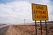 Traffic sign with impacts of gun buckshot reading USE EXTREME CAUTION in the New Mexico desert.