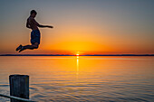Junge springt vom Holzsteg ins Wasser bei Sonnenuntergang, Chieming, Chiemsee, Chiemgau, Bayern, Deutschland, Europa