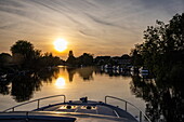 Bow of a Le Boat Horizon 4 houseboat on the River Thames with reflection of trees at sunset, Chertsey, Surrey, England, United Kingdom
