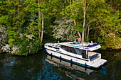 Aerial view of a Le Boat Horizon 4 houseboat moored to an island on the River Thames near Cliveden National Trust, with people preparing a barbecue dinner on deck, near Maidenhead, Berkshire, England, United Kingdom