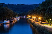 Houseboats moored on Canal de la Marne au Rhin with town at dusk, Lutzelbourg, Moselle, France