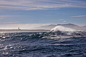 Breaking wave in the South Atlantic with a view of Danger Point Lighthouse, near Gansbaai, Western Cape, South Africa
