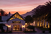 Exterior view of Ulumbaza Wine Bar(s) at Springfontein Wine Estate with palm trees and mountains at sunset, Stanford, Western Cape, South Africa