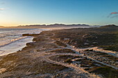 Aerial view of people riding fat tire bicycles at sunset on sandy paths along the coast and beach in Walker Bay Nature Reserve, Gansbaai De Kelders, Western Cape, South Africa