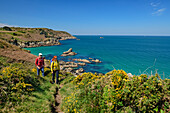 Man and woman hiking on the Zöllnerweg at Cap Sizun with the sea and rocky islands in the background, Cap-Sizun, GR 34, Zöllnerweg, Brittany, France