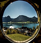 Blick durch einen Rahmen vom Kalvarienberg auf St. Wolfgang, den Wolfgangsee und die Berge des  Salzkammerguts, Österreich
