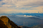 Luftaufnahme über eine wunderschöne Berglandschaft und einen Berggipfel mit Menschen und mit schwebenden Wolken und schneebedecktem Monte Rosa an einem sonnigen Tag im Tessin, Schweiz